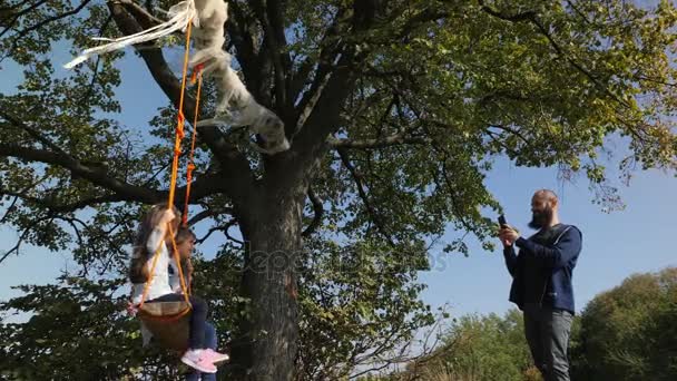 Vader foto van zijn twee dochters swingen op een schommel onder een boom. - Video