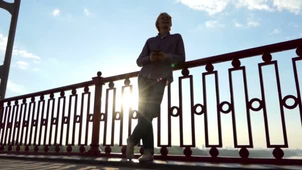Jonge blonde Man geniet van prachtige zonsondergang op een rivier brug Over de Dnipro in Slo-Mo - Video
