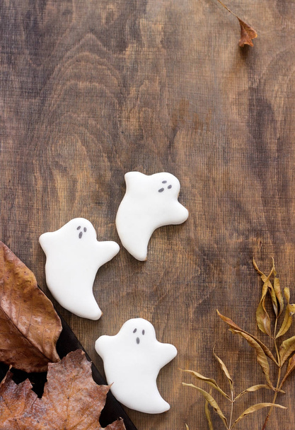 Fantasma de pan de jengibre para Halloween, decorado con hojas de otoño, sobre un fondo de madera
. - Foto, imagen