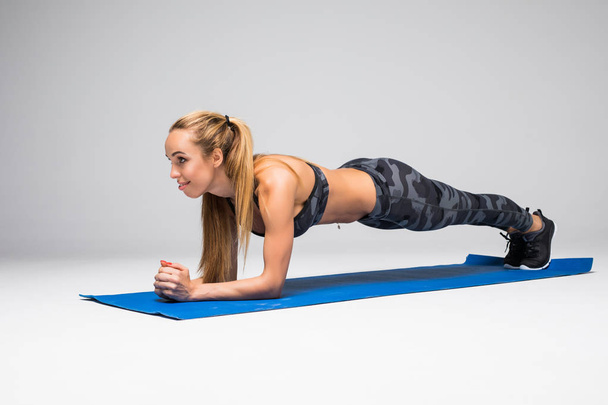 Young attractive woman practicing yoga, standing in Push ups or press ups exercise, Plank pose, working out, wearing sportswear bra and pants, full length, gray studio background - Photo, Image