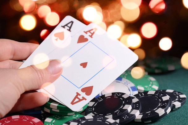 Casino chips en paar azen in een croupiers hand tegen heldere bokeh lichten. Poker spel thema concept. - Foto, afbeelding