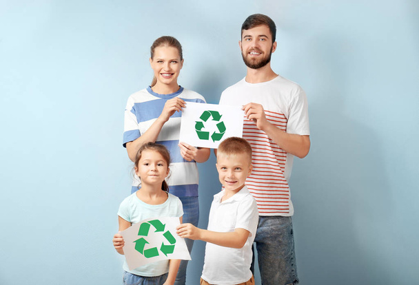 Family holding paper sheets with recycling symbol on color background - Фото, изображение