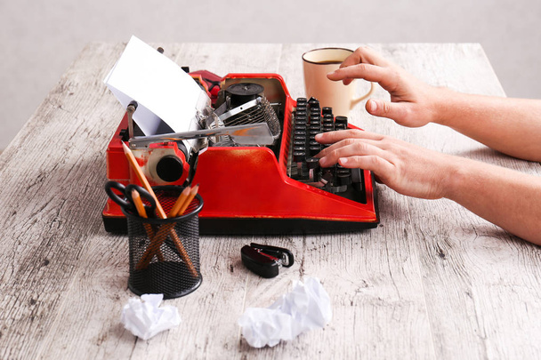 La machine à écrire est rouge avec du papier dedans et sur la table
 - Photo, image