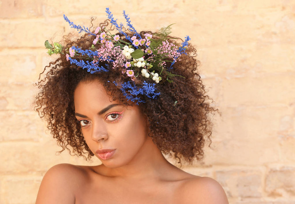 Beautiful young African-American woman with flowers in hair against brick wall - Fotografie, Obrázek