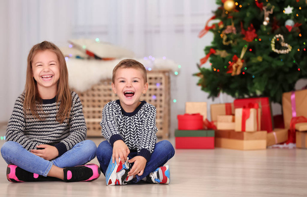 Cute little children sitting on floor in room decorated for Christmas - 写真・画像