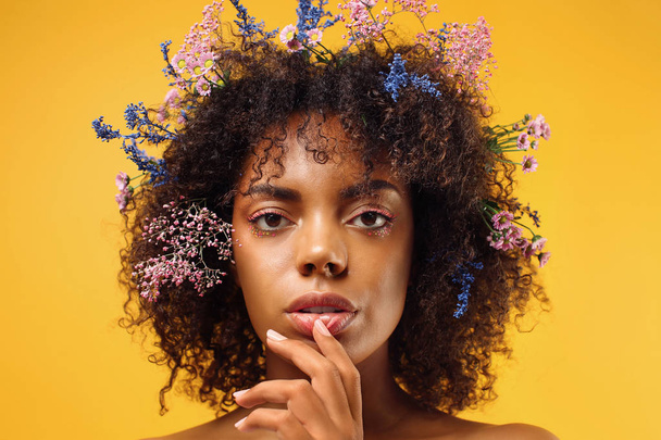 Beautiful young African-American woman with flowers in hair against color background - Foto, immagini