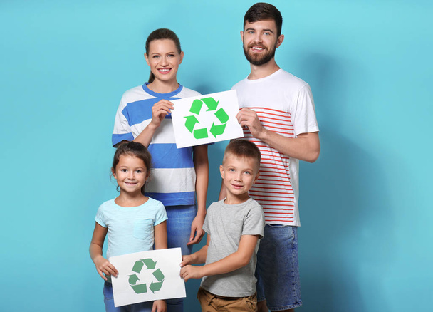 Family holding paper sheets with recycling symbol on color background - Photo, image