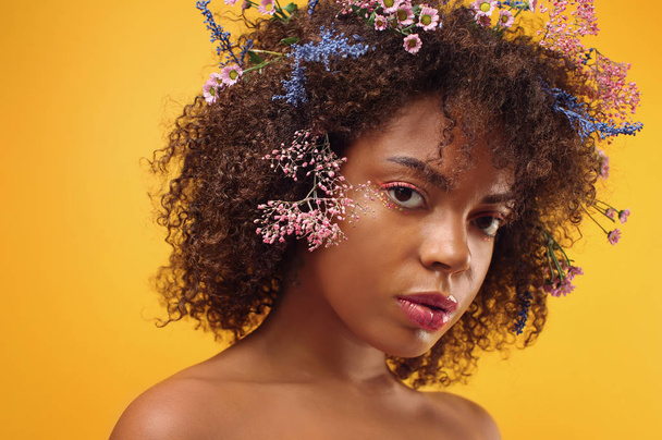 Beautiful young African-American woman with flowers in hair against color background - Foto, imagen
