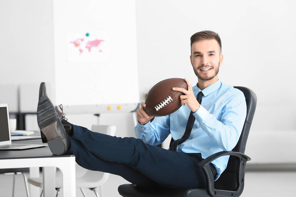 Young handsome man with ball for American football in office - Zdjęcie, obraz