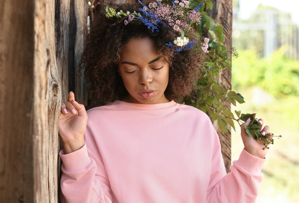 Beautiful young African-American woman with flowers outdoors - Фото, зображення