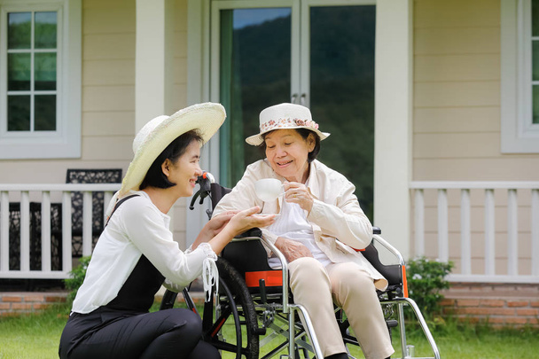 Mujer mayor relajarse en silla de ruedas en el patio trasero con su hija
 - Foto, imagen
