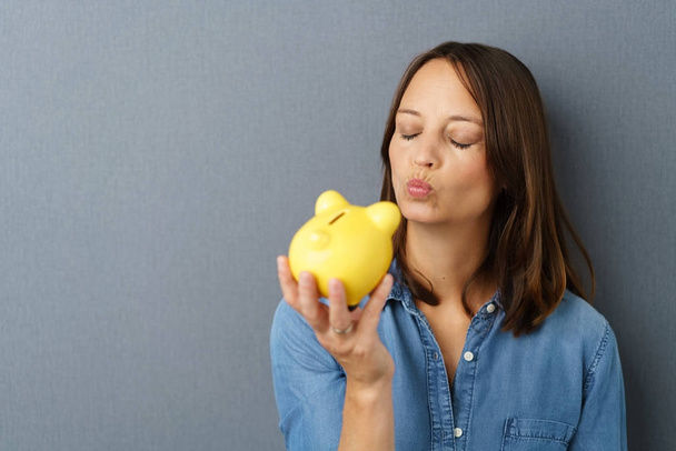 Young smiling woman kissing piggy bank - Foto, afbeelding