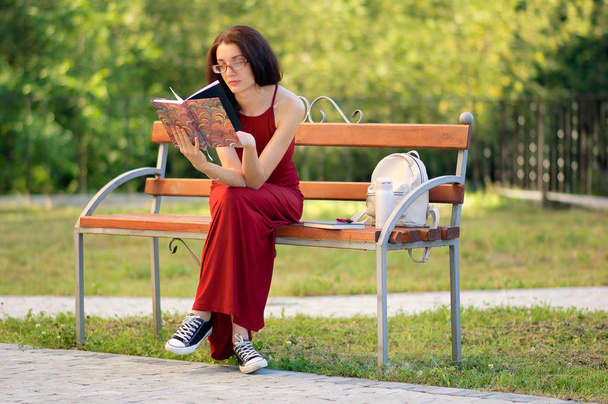 Портрет молодой женщины в казуальной одежде, читающей книгу в городском парке в солнечный теплый летний день
. - Фото, изображение