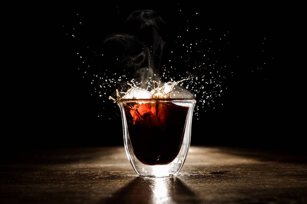 Hot and aromatic coffee spilling from transparent glass cup - Foto, imagen