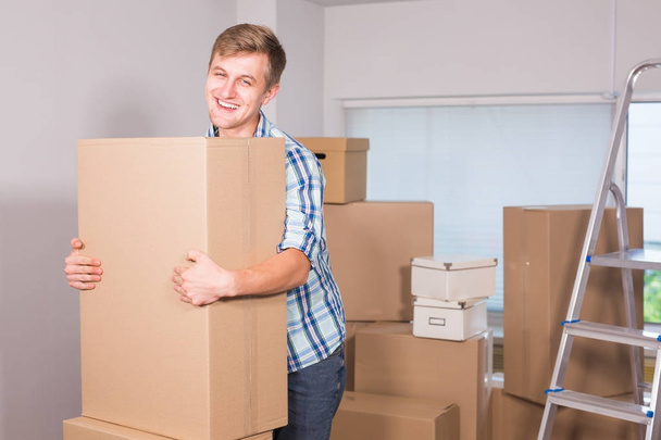 Stěhování do nového bytu. Veselý mladý muž, držící kartonových krabic a usmívá se na kameru, zatímco ostatní lepenkových krabic na pozadí. - Fotografie, Obrázek