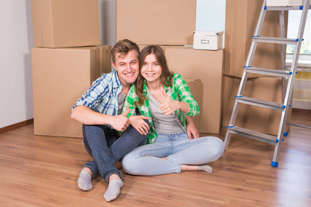 Переїзд в новий будинок і ремонт в квартирі. Любов пара показує великий палець вгору і сидить у порожній квартирі серед коробок
 - Фото, зображення