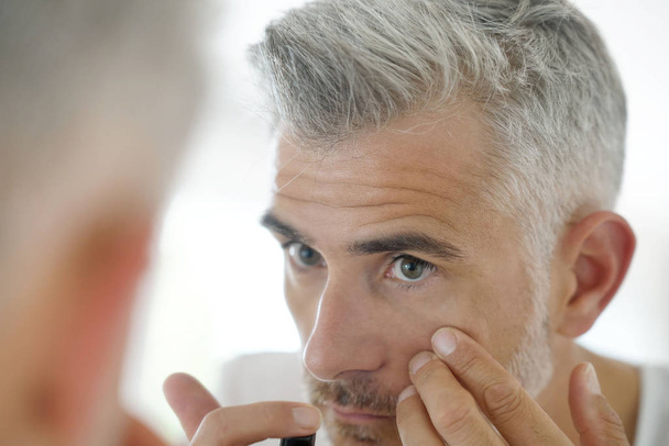 Middle-aged man applying cosmetic - 写真・画像