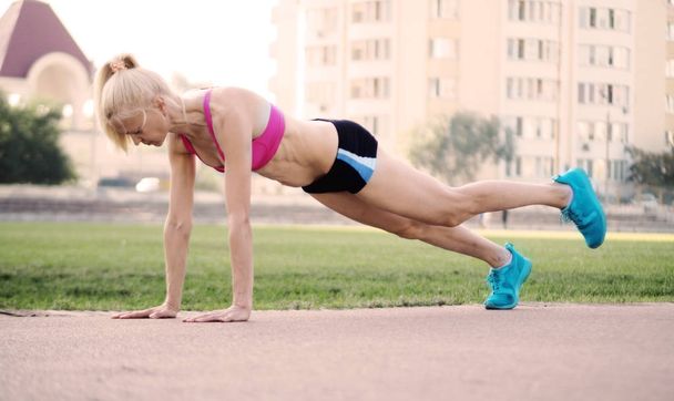 Piękny fitness kobieta robi deski stretch odkryty na stadionie - Zdjęcie, obraz