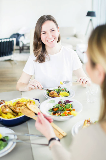 Two happy women having dinner together with roasted chicken, potato, green salad - Fotoğraf, Görsel