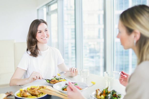 Two young women having dinner together at home. Women eating together - 写真・画像
