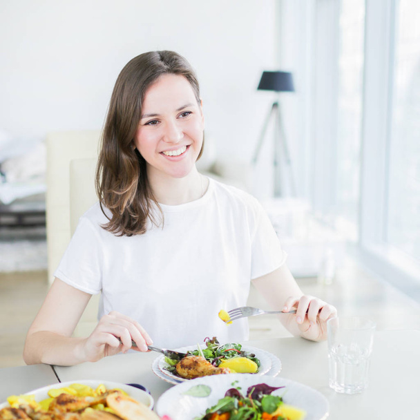 Beautiful cheerful woman eating salad with chicken at the table in modern apartment - Foto, Imagen