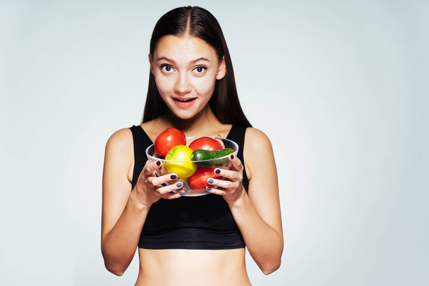 een jonge mooie sport meisje in een zwarte top houdt spoor van haar gewicht en figuur, bezit is een plaat met nuttig groenten en vruchten in haar handen - Foto, afbeelding
