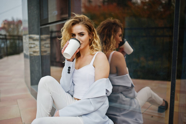 Stijlvolle krullend blond model meisje dragen op wit met kopje koffie - Foto, afbeelding