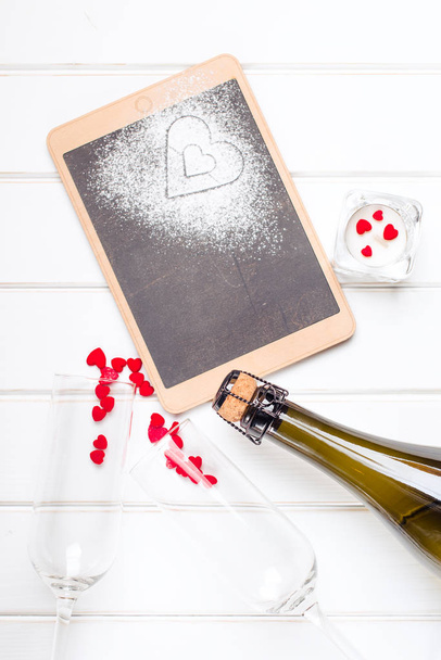 Two glasses, champagne and chalkboard with decorative hearts on white wooden background. Valentines day card. - Photo, Image