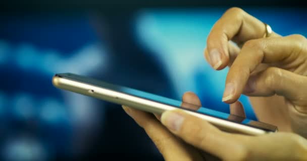Zbliżenie ręki kobiece pisania wiadomości na smart telefonu na tle ekranu Tv. - Materiał filmowy, wideo
