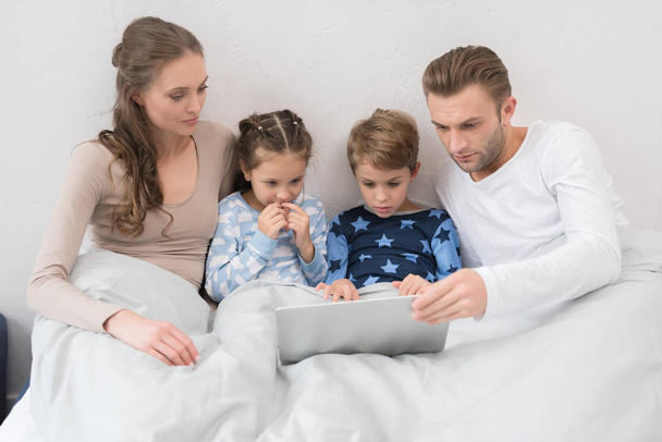 Famiglia sdraiata a letto con laptop
 - Foto, immagini