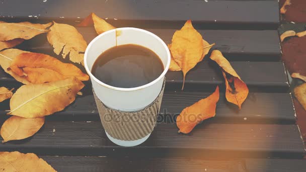 Kaffee zum Mitnehmen. Kaffee to go auf einer Bank mit gelben Blättern im Herbstpark. 4k Video. getönt mit Kinoeffekten. - Filmmaterial, Video