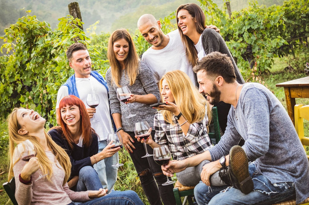 Happy friends having fun outdoor - Young people drinking red wine at harvest time in farmhouse vineyard winery - Youth friendship concept with mates using smartphone for a live mobile phone call - Foto, Imagem