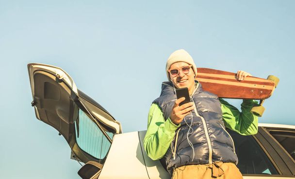 モバイルのスマートと流行に敏感な若いハンサムな男電話車旅で音楽を聴く - 現代の技術概念と放浪旅行ライフ スタイル - 秋冬青年代替ファッション - レトロな色調 - 写真・画像