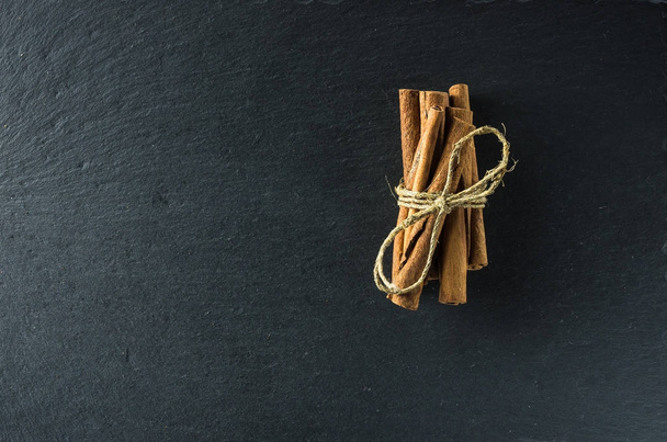 Cinnamon in sticks tied with a coarse string lies on a slate board from above - Photo, Image