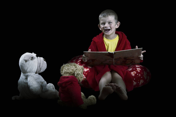 Funny boy with stuffed animals reading a book before bed time ar - Foto, afbeelding