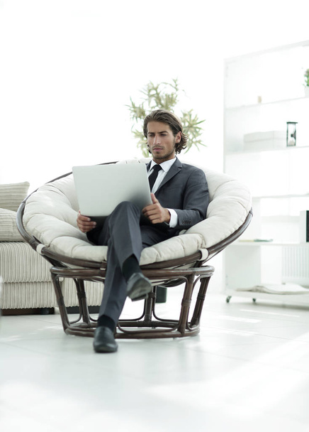 young businessman with laptop sitting in big comfortable armchair. - Zdjęcie, obraz