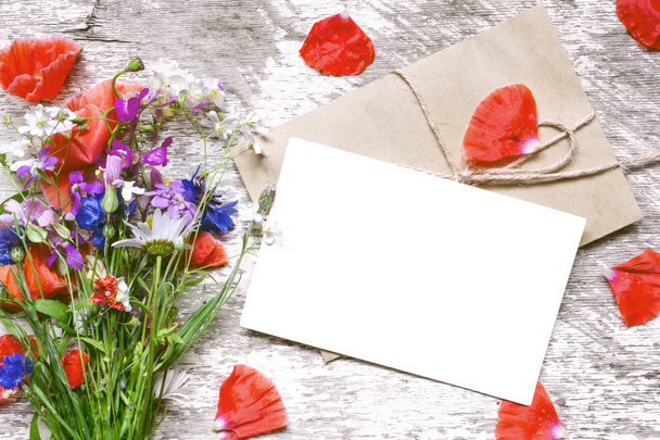 tarjeta de felicitación blanca en blanco con ramo de flores silvestres y sobre con pétalos de flores
 - Foto, imagen