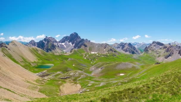 Panorama from above on high altitude mountain peaks, green meadows and blue lake in idyllic uncontaminated environment once covered by glaciers. Summer adventures and exploration on the Italian French Alps. - Footage, Video