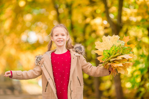 Portrait of adorable little girl with yellow leaves bouquet in fall - Photo, Image