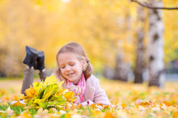 Портрет чарівної дівчинки з жовтим листям букета восени. Красива усміхнена дитина лежить на килимі
 - Фото, зображення