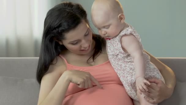 Woman pregnant with child holding infant, pointing to stomach, baby looking down - Imágenes, Vídeo