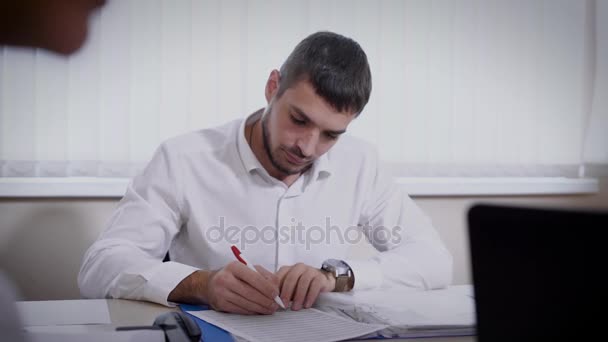 Elegant male office employee working on important documents at desk - Filmati, video