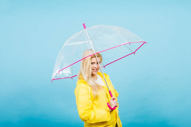 Happy woman wearing raincoat holding transparent umbrella - Foto, imagen