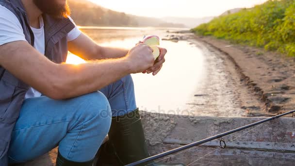 Νεαρός ψαράς τρώει ένα μήλο που κάθεται σε μια αλιευτική βάρκα στον ποταμό. Ζεστό ήλιο-καλοκαιρινό βράδυ - Πλάνα, βίντεο