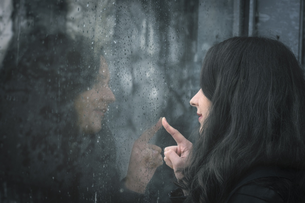 Mujer y su reflejo en ventana lluviosa
 - Foto, Imagen