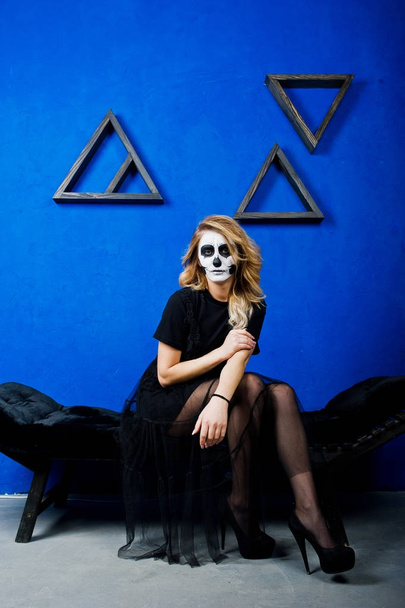 Halloween Totenkopf Make-up Mädchen tragen in schwarz gegen blaue Wand bei  - Foto, Bild