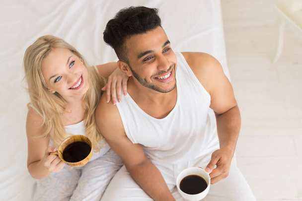 Молода пара п'є каву сидячи в ліжку, щаслива посмішка іспаномовний чоловік і жінка зверху кут зору
 - Фото, зображення