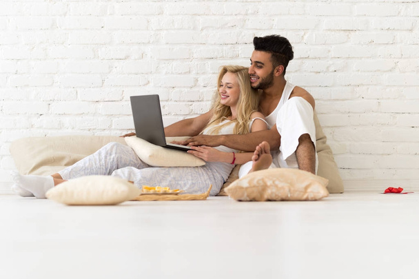 Casal jovem sentar-se no chão travesseiros, homem hispânico e mulher usando computador portátil amantes quarto
 - Foto, Imagem
