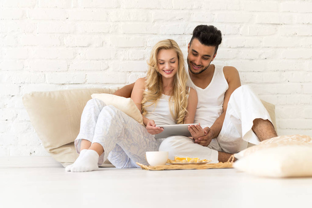 Young Couple Sit On Pillows Floor, Hispanic Man And Woman Using Tablet Computer Lovers Bedroom - Фото, изображение