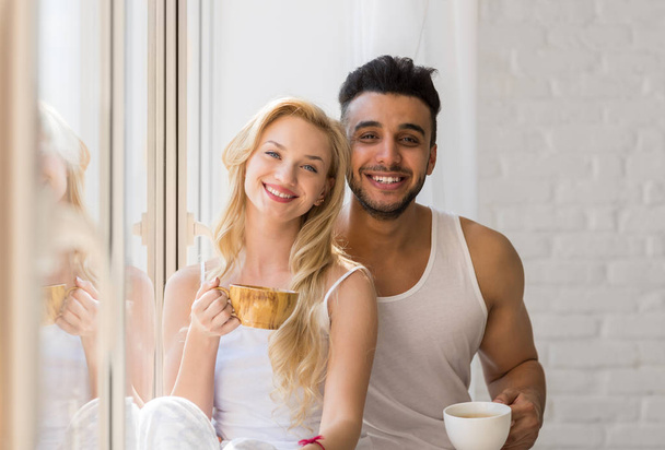 Young Beautiful Couple Stand Near Big Window, Drink Morning Coffee Cup, Happy Smile Hispanic Man Woman - Foto, immagini